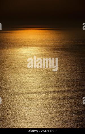 Abstrakte Seebrücke bei Sonnenuntergang mit glitzerndem Sonnenlicht, das vom sanft kreischenden Wasser reflektiert wird. Stockfoto