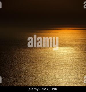 Abstrakte Seebrücke bei Sonnenuntergang mit glitzerndem Sonnenlicht, das vom sanft kreischenden Wasser reflektiert wird. Stockfoto