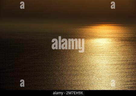 Abstrakte Seebrücke bei Sonnenuntergang mit glitzerndem Sonnenlicht, das vom sanft kreischenden Wasser reflektiert wird. Stockfoto