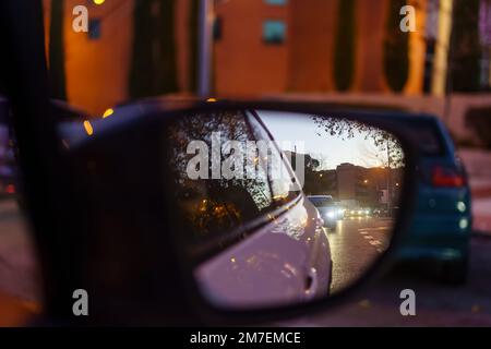 Rückspiegel eines Autos bei Nacht, der die Lichter anderer Fahrzeuge reflektiert, die auf der Straße herumfahren. Stockfoto