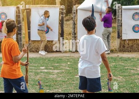 Rückansicht der asiatischen Jungen tragen Gesichtsmaske zielt Bogenschießen Bogen und Pfeil zu bunten Ziel im Schießstand während des Trainings und des Wettbewerbs. Übung und Co Stockfoto