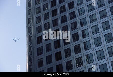 Ein Düsenflugzeug überquert den Kopf cloe zur stell-verkleideten Struktur des Al arge Skyscrpaer in London. canary Wharf. Stockfoto