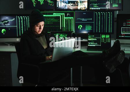 Informative Hacker-Frau, die Code auf dem Laptop tippt, im Hintergrund viele Computerbildschirme mit Daten. Junge Programmiererin, die einen Firewall-Angriff oder Phishing mit dem Internet durchführt. Cybersicherheitskonzept. Hochwertiges Foto Stockfoto
