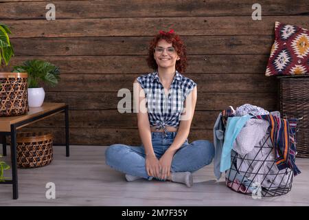 Ein lächelndes Mädchen in einem karierten Hemd sitzt auf dem Boden neben der Wäscherei. Stockfoto