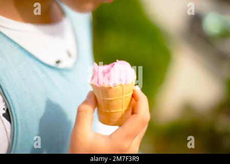 Rosa Eis in einem Waffelbecher, abgebissen und in den Händen eines Kindes geschmolzen. Stockfoto