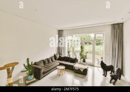 Ein Wohnzimmer mit zwei Sofas und einer Katze, die auf dem Boden vor dem Fenster mit Blick auf den Garten sitzt Stockfoto