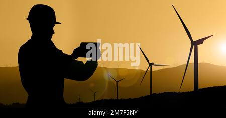 Silhouette eines Ingenieurs mit Tablet-Computer und Windturbinen bei Sonnenuntergang Stockfoto