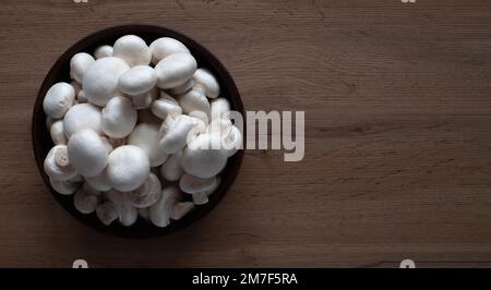 Frische weiße Pilze in einer Schüssel auf einem hölzernen Tisch. Stockfoto