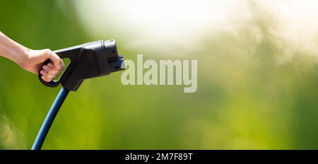 Hand mit Ladestecker für Elektroauto auf grünem Hintergrund Stockfoto