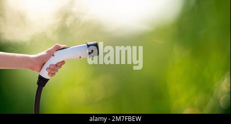 Hand mit Ladestecker für Elektroauto auf grünem Hintergrund Stockfoto