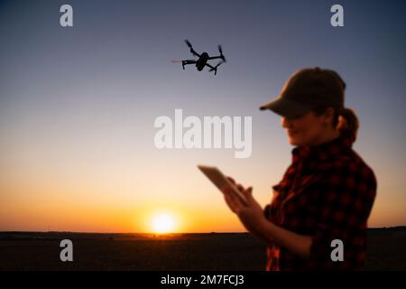 Der Bauer steuert die Drohne mit einem Tablet bei Sonnenuntergang. Intelligente Landwirtschaft und Präzisionslandwirtschaft Stockfoto