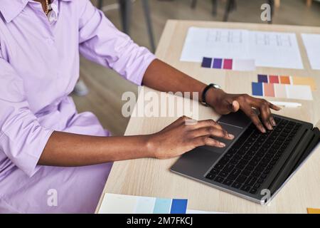 Seitliche Nahaufnahme einer schwarzen jungen Frau, die während der Arbeit an einem Designprojekt ein Notebook benutzt Stockfoto