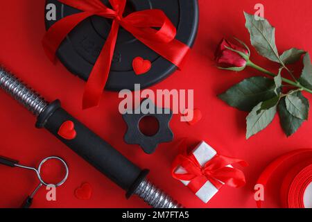 Hantelglocke, Gewichtsteller, rote Rose und Verlobungsring. Liebesgeschenk zum Valentinstag, Geburtstag, Jubiläum oder zur Hochzeit. Stockfoto