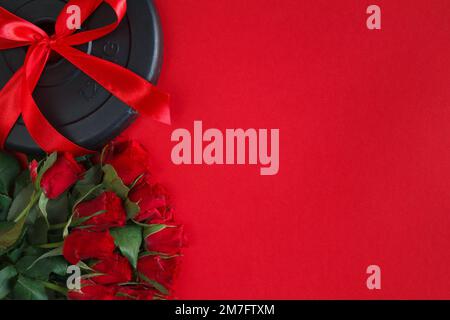 Gewichtsteller mit Kurzhantel und roten Rosen. Liebesgeschenk zum Valentinstag, Geburtstag, Hochzeitstag, Hochzeit. Flach liegend mit Kopierbereich. Stockfoto