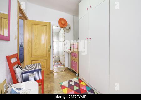 Kinderzimmer mit Kommode mit Rollen und farbigen Schubladen und vierteiligem Kleiderschrank aus weißem Holz, einem farbigen Teppich und einem Spiegel mit Lean-Effekt Stockfoto