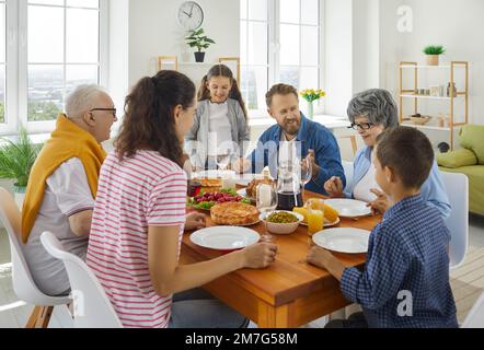 Familieneltern, Großeltern und Kinder, die zu Mittag essen und sich am Tisch unterhalten. Stockfoto