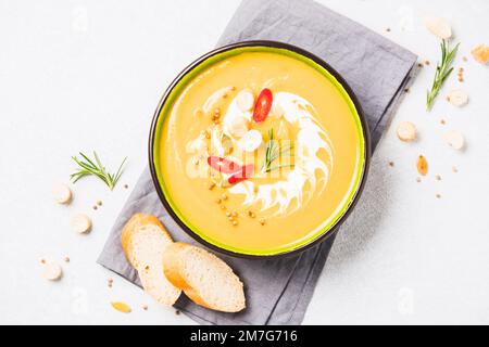 Würzige Kürbiscreme-Suppe garniert mit Croutons und rotem Chili-Pfeffer. Dicke Butternusskürbis-Bisque in grüner Schüssel auf weißem Tisch. Minimalistischer Style. Sele Stockfoto