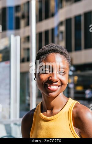 Porträt einer fröhlichen afro-amerikanischen jungen Frau, die an einem sonnigen Tag in die Kamera schaut. Sie trägt ein gelbes Sommerhemd Stockfoto