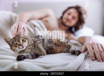 Ein junger Mann, der im Bett mit einer süßen Katzenkatze kuschelt Stockfoto