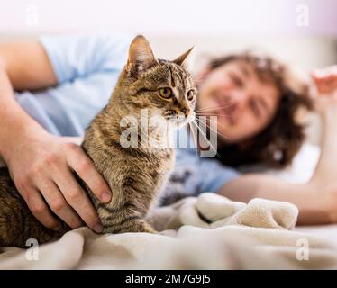 Ein junger Mann, der im Bett mit einer süßen Katzenkatze kuschelt Stockfoto