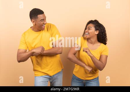Das Leben genießen. Glückliche, sorgenfreie schwarze Ehepartner, die tanzen und Spaß haben, sich anschauen und lächeln, gelber Hintergrund Stockfoto