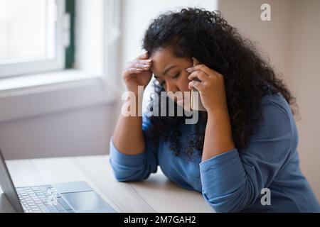 Verärgerte junge Frau, die am Schreibtisch sitzt und online an einem Laptop arbeitet Stockfoto