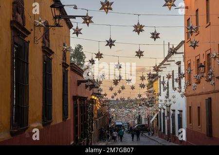 Farbenfrohe Verzierungen aus Zinn, die sich bei Sonnenuntergang über historischen Gebäuden in der Hidalgo Street erstreckten, um das neue Jahr im historischen Viertel zu feiern, am 4. Januar 2023 in San Miguel de Allende, GTO, Mexiko. Stockfoto