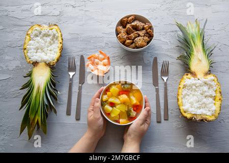Asiatischer Reis in geschnitzter Ananas mit Garnelen und Hühnern auf grauem Hintergrund, Draufsicht. Köstliches tropisches Gericht. Stockfoto