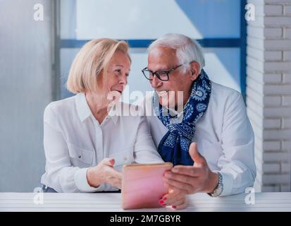 Ein paar Großeltern, die Spaß auf der Terrasse haben, während sie ein Tablet benutzen. Sie sind glücklich. Glück und Alterskonzept. Stockfoto