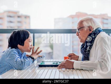 Großvater und Enkel spielen ein Brettspiel auf der Terrasse. Sie amüsieren sich. Adoption und Familienkonzept. Stockfoto