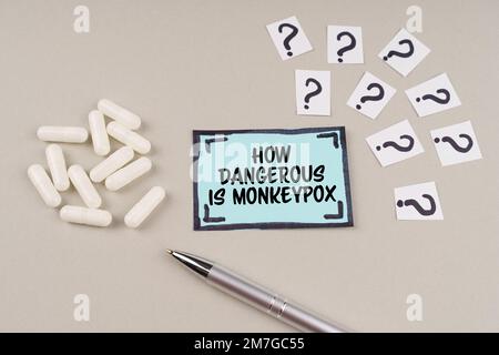 Medizinisches Konzept. Auf einer grauen Oberfläche befinden sich Fragezeichen und ein blauer Aufkleber mit der Inschrift - wie gefährlich sind Affen-Pocken Stockfoto
