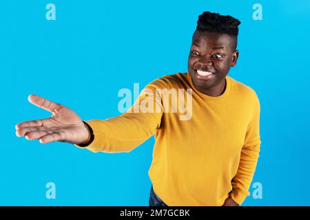 Aufgeregter afroamerikanischer Mann, der sich die Hand ausstreckt und ein unsichtbares Objekt auf seiner Handfläche hält Stockfoto