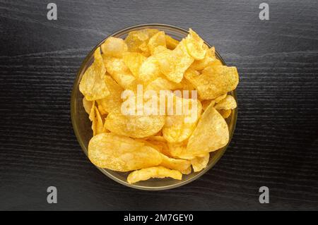 Draufsicht einer Schüssel Kartoffelchips auf schwarzem Hintergrund. Konzept der Snackkost. Stockfoto