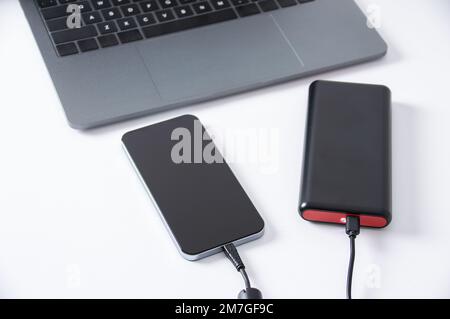 USB-Ladegerät mit Powerbank an Smartphone angeschlossen, Mobiltelefonakku auf dem Schreibtisch im Büro. Stockfoto