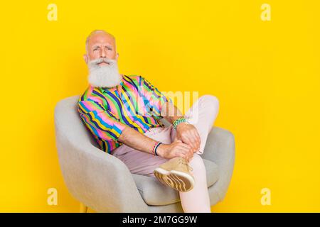 Porträt eines fokussierten, selbstbewussten alten Menschen Sessel Sessel mürrisches Gesicht isoliert auf gelbem Hintergrund Stockfoto