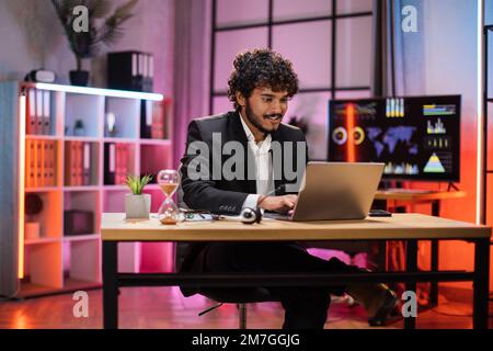Porträt eines gutaussehenden, erfahrenen, schlauen, schlauen, schlauen Geschäftsmanns, der am Tisch sitzt und abends in einem modernen Büro einen Laptop benutzt. Stockfoto