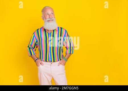 Porträt eines lustigen alten Mannes mit langem Bart Tragen Sie farbenfrohe Hemdarme in Taschen sehen leerer Raum isoliert auf gelbem Hintergrund aus Stockfoto