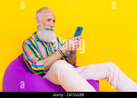 Foto eines fröhlichen positiven Mannes trägt ein farbenfrohes Hemd Tippen Apfel samsung Modern Gadget empty space isolierter gelber Hintergrund Stockfoto