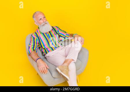 Das Porträt eines gutaussehenden älteren Menschen, der bequem sitzt, sieht leerer Raum aus, isoliert auf gelbem Hintergrund Stockfoto