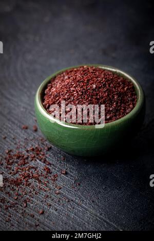 Getrocknetes gemahlenes rotes Sumac-Pulver in einer grünen Schüssel auf dunklem Hintergrund. Stockfoto