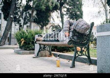 Ein Obdachloser, der auf einer Bank schläft. Armer Bettler auf der Straße der Stadt. Stockfoto