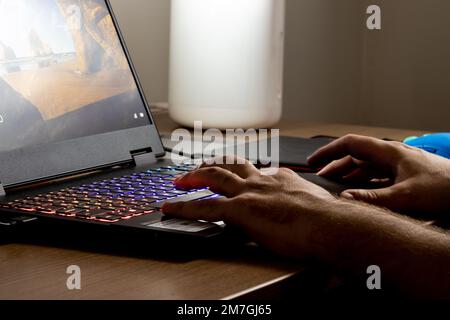 Ein weißer Mann, der vor dem Notebook arbeitet, während die Gamer-Lichter leuchten. Stockfoto