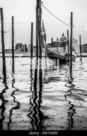 Eine Graustufenaufnahme eines hölzernen Ruderboots, das an einen Holzpfosten im Wasser gebunden ist Stockfoto