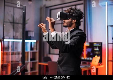 Junge männliche Mitarbeiter, die während eines Meetings im Bürozimmer ein VR-Headset tragen. Selbstbewusster bärtiger Mann in formeller Kleidung mit innovativer Technologie während der Geschäftsstrategie. Stockfoto