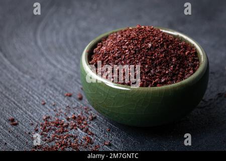 Getrocknetes gemahlenes rotes Sumac-Pulver in einer grünen Schüssel auf dunklem Hintergrund. Stockfoto