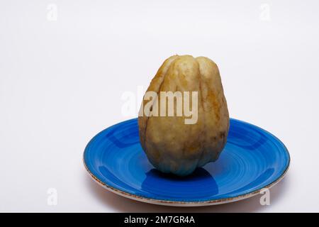 Nahaufnahme eines auf weißem Hintergrund isolierten Chayoten auf einer blauen Keramikplatte Stockfoto