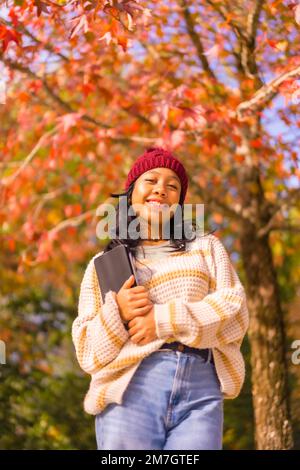 Porträt eines asiatischen Mädchens im Herbst mit einem lächelnden Tablet in einem Wald aus roten Blättern, Technologiekonzept Stockfoto