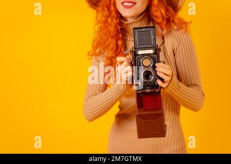 Unerkennbare Rothaarige auf gelbem Hintergrund, Kopierraum, mit einer alten Fotokamera