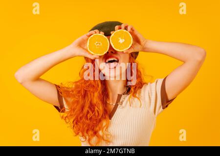 Teenager Rothaarige hält eine Orange über einen isolierten gelben Hintergrund und bedeckt ihre Augen Stockfoto