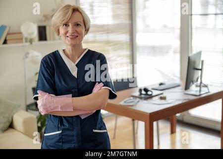 Porträt eines lächelnden Senior Housekeeping, das in der Wohnung steht und in die Kamera schaut Stockfoto